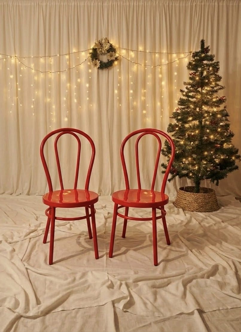 The chair set: two red bentwood chairs on a cream drop, beside a lit Christmas tree, with a fairy-light curtain and a wreath behind