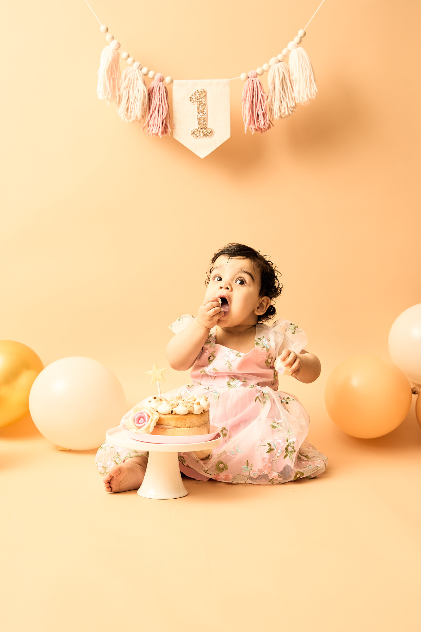 One-year-old girl tasting icing from her fingers during a first birthday cake smash session