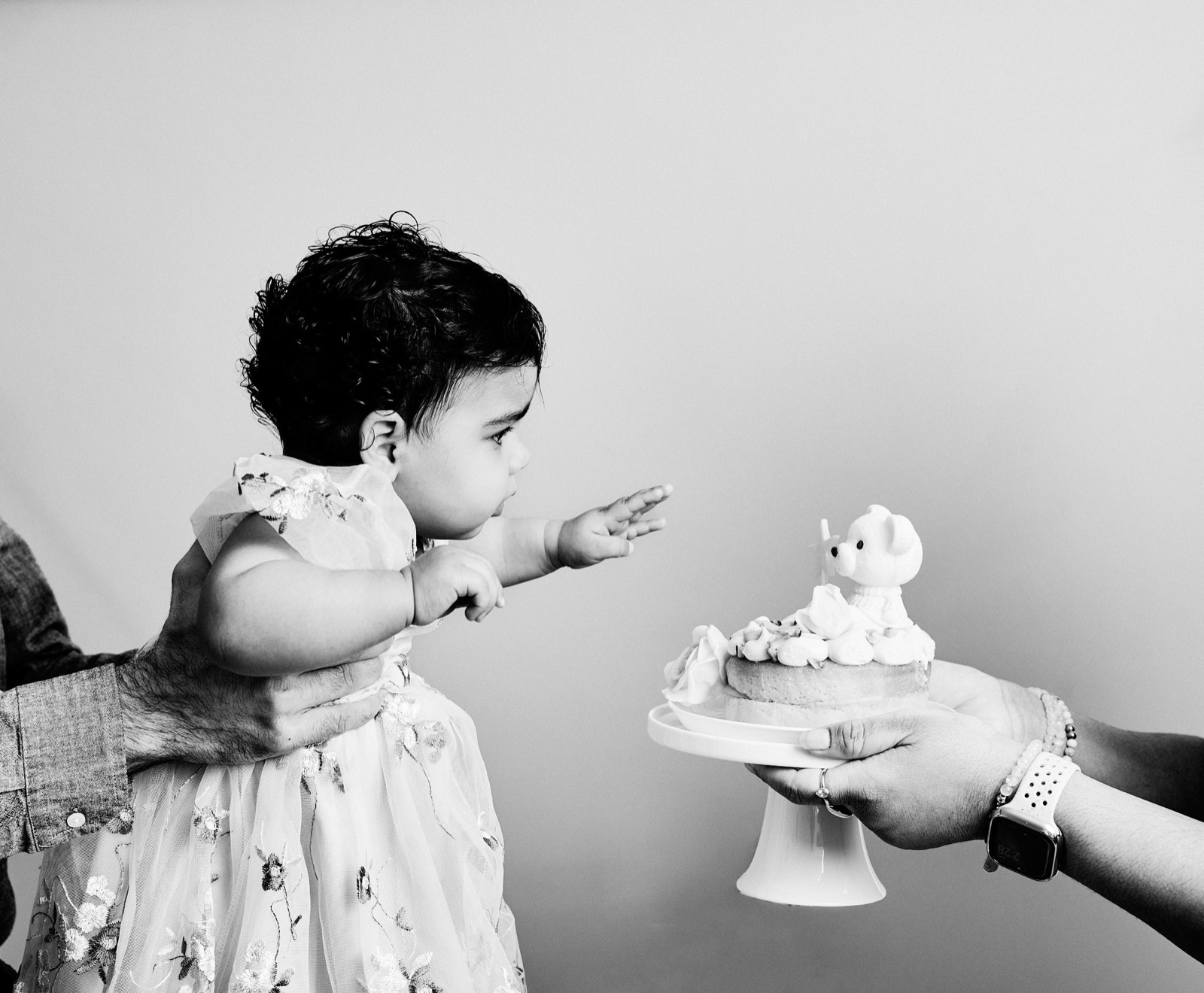 Black and white photo of a one-year-old reaching out cautiously to touch her smash cake for the first time