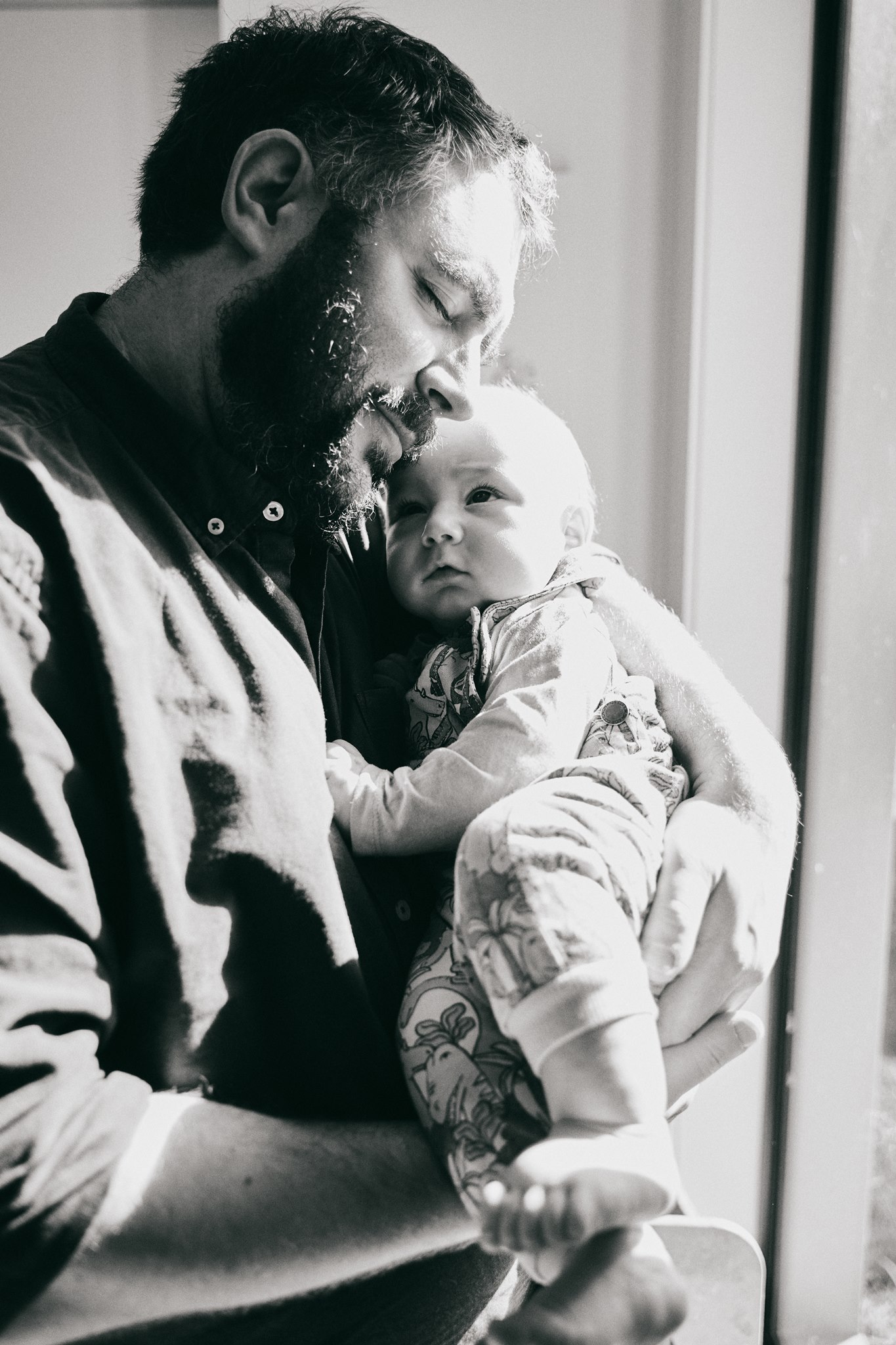 Dad holding his newborn close against his chest, black and white in-home newborn portrait