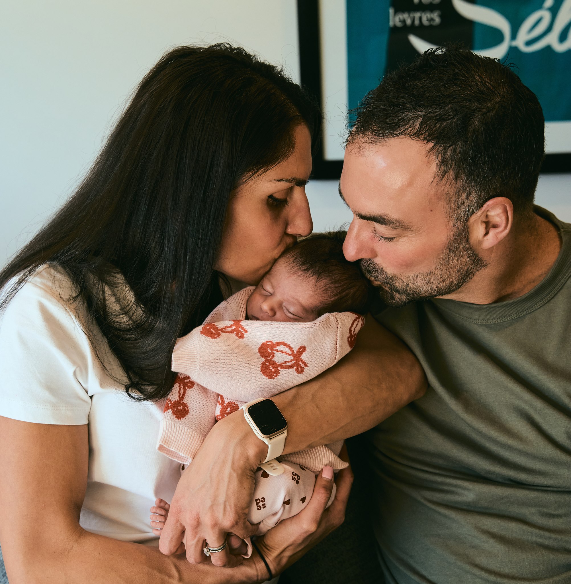 Parents kissing while cuddling their two children together on the couch, relaxed in-home family session
