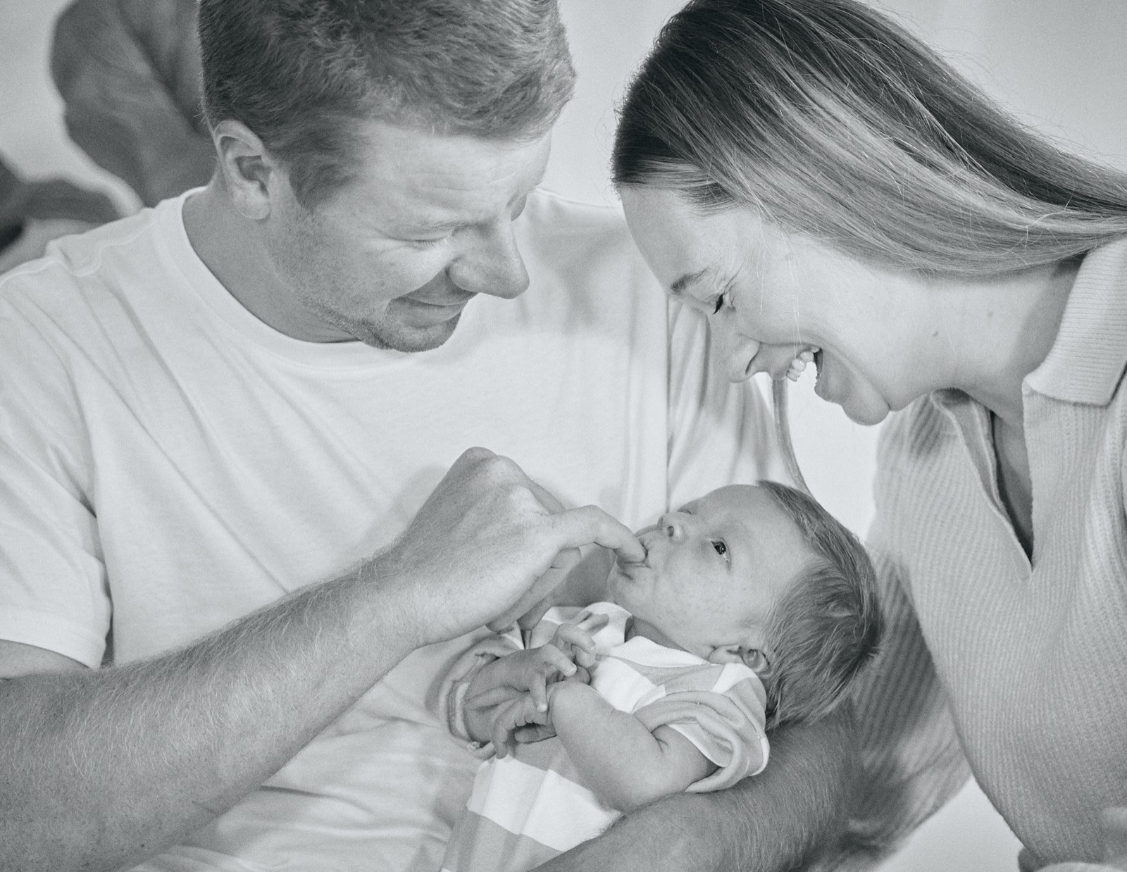 Black and white photo of parents kissing while holding their newborn