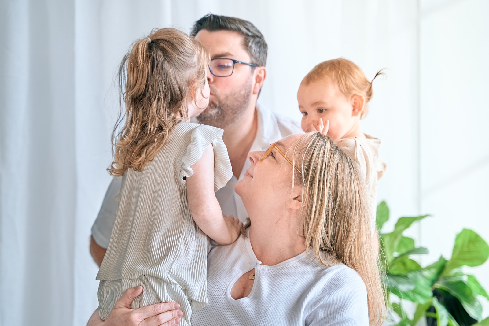 Mum kissing her toddler while holding the baby, everyday family chaos captured