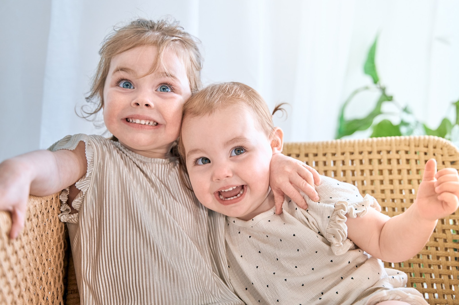 Two young sisters giggling together in a wicker chair