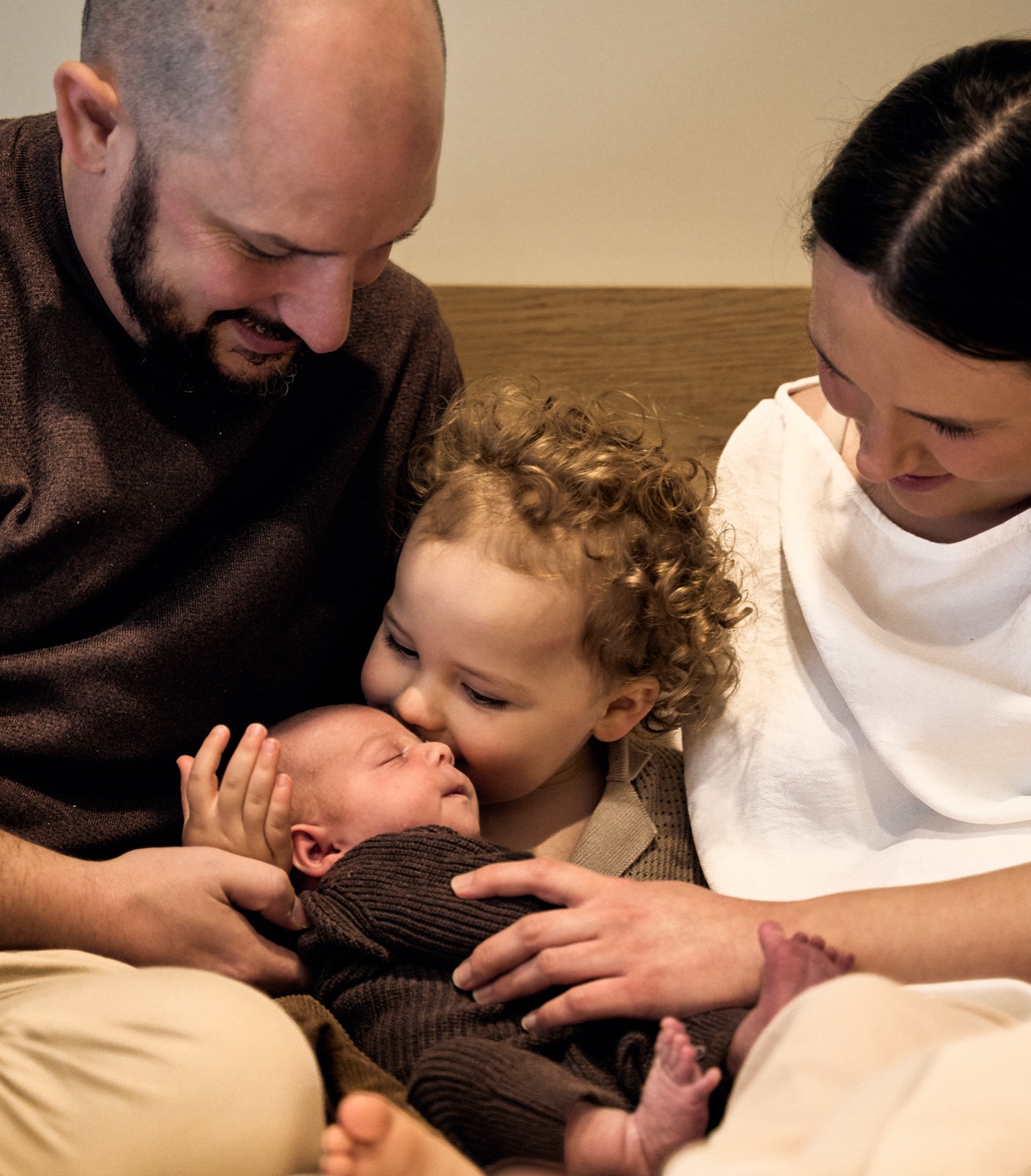 Big sister leaning in for a kiss while dad holds the new baby