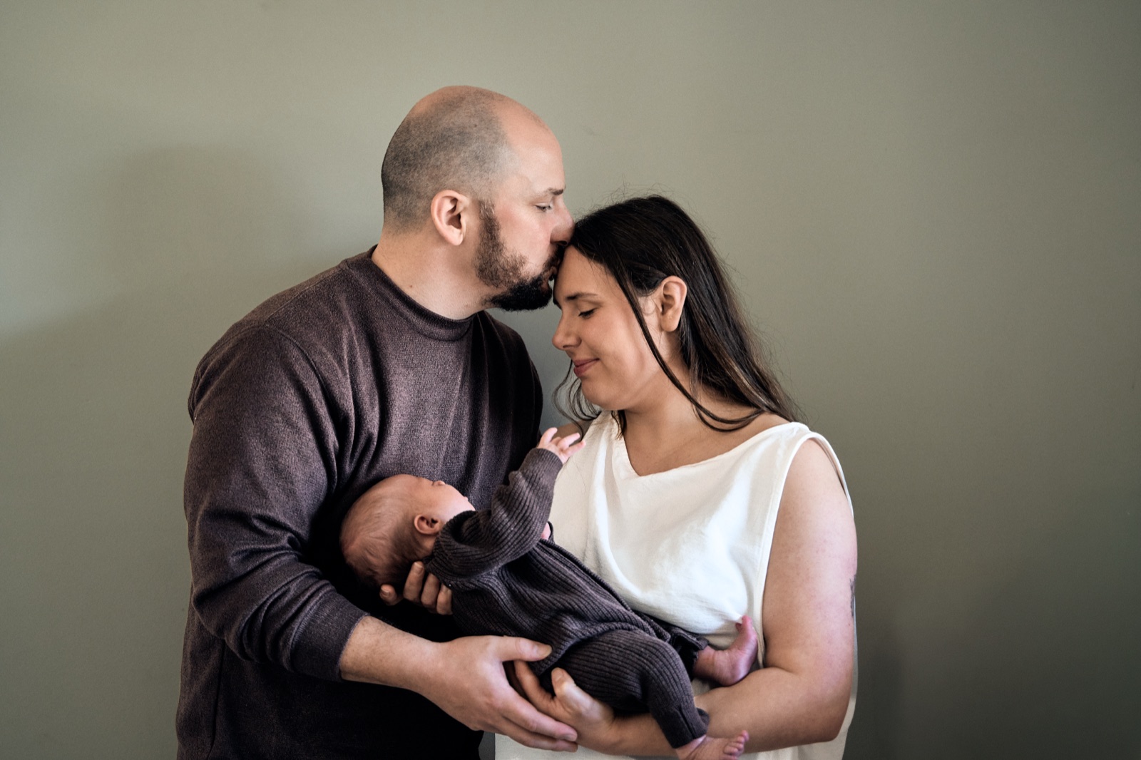 Parents gazing down at their sleeping newborn in soft window light