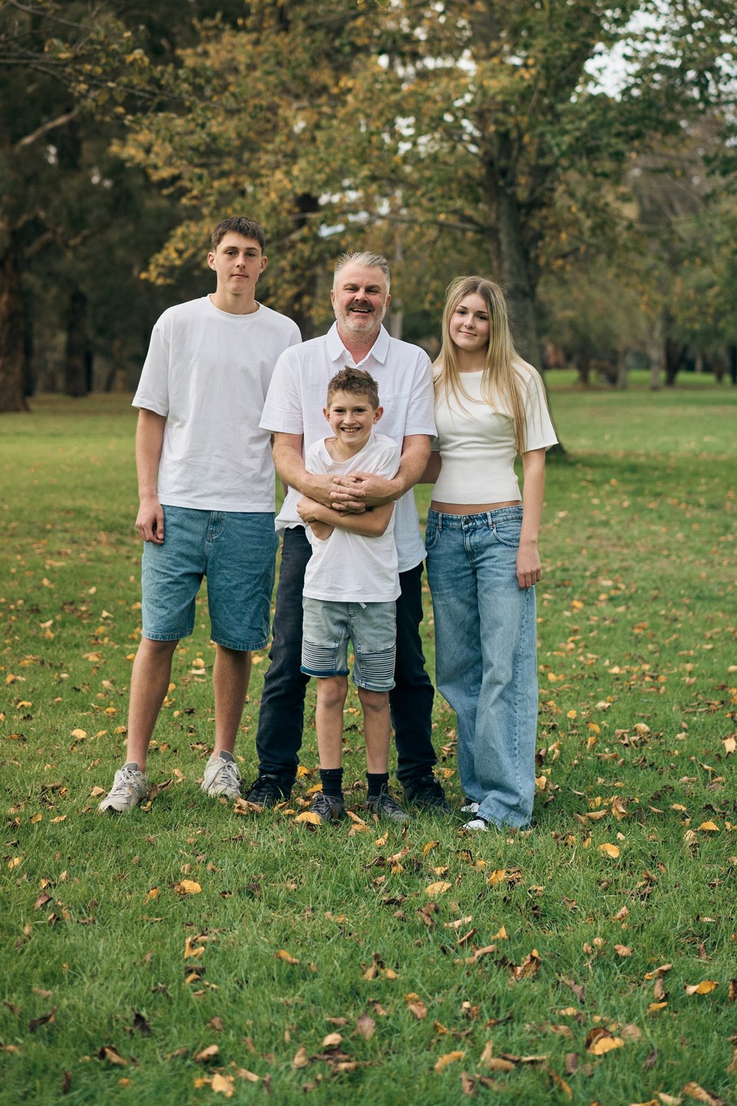 Dad with his three kids, arms around each other in the park
