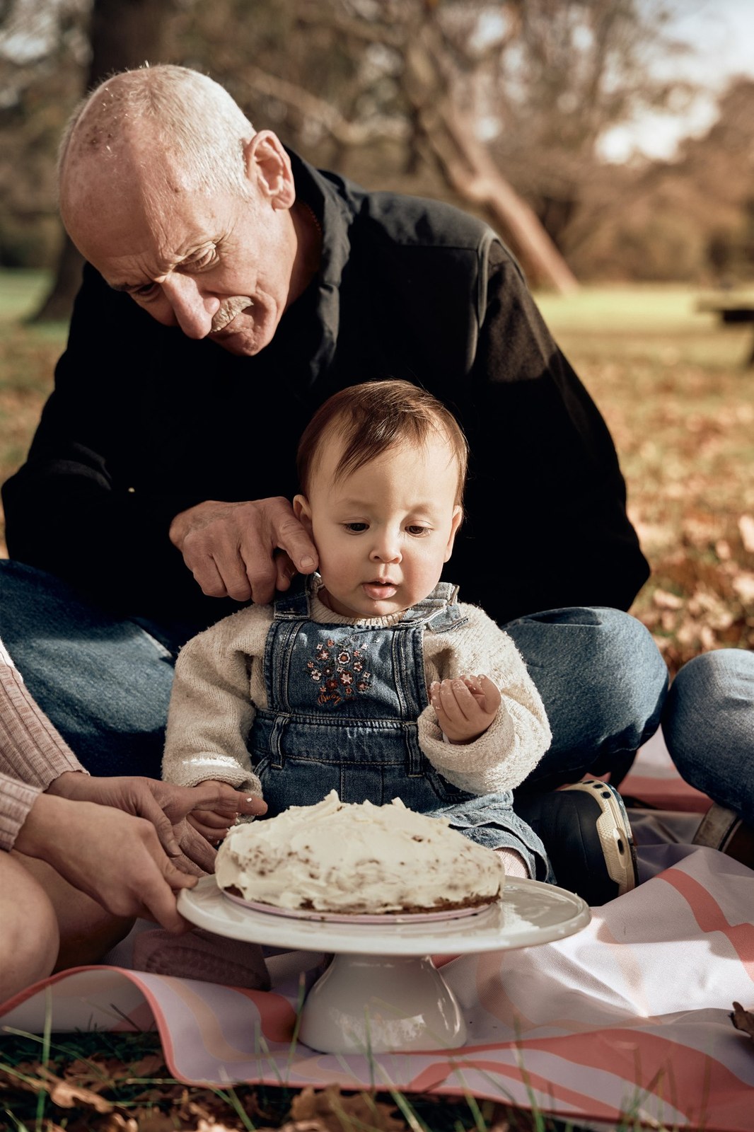 Grandad helping his grandson with his first birthday cake outdoors