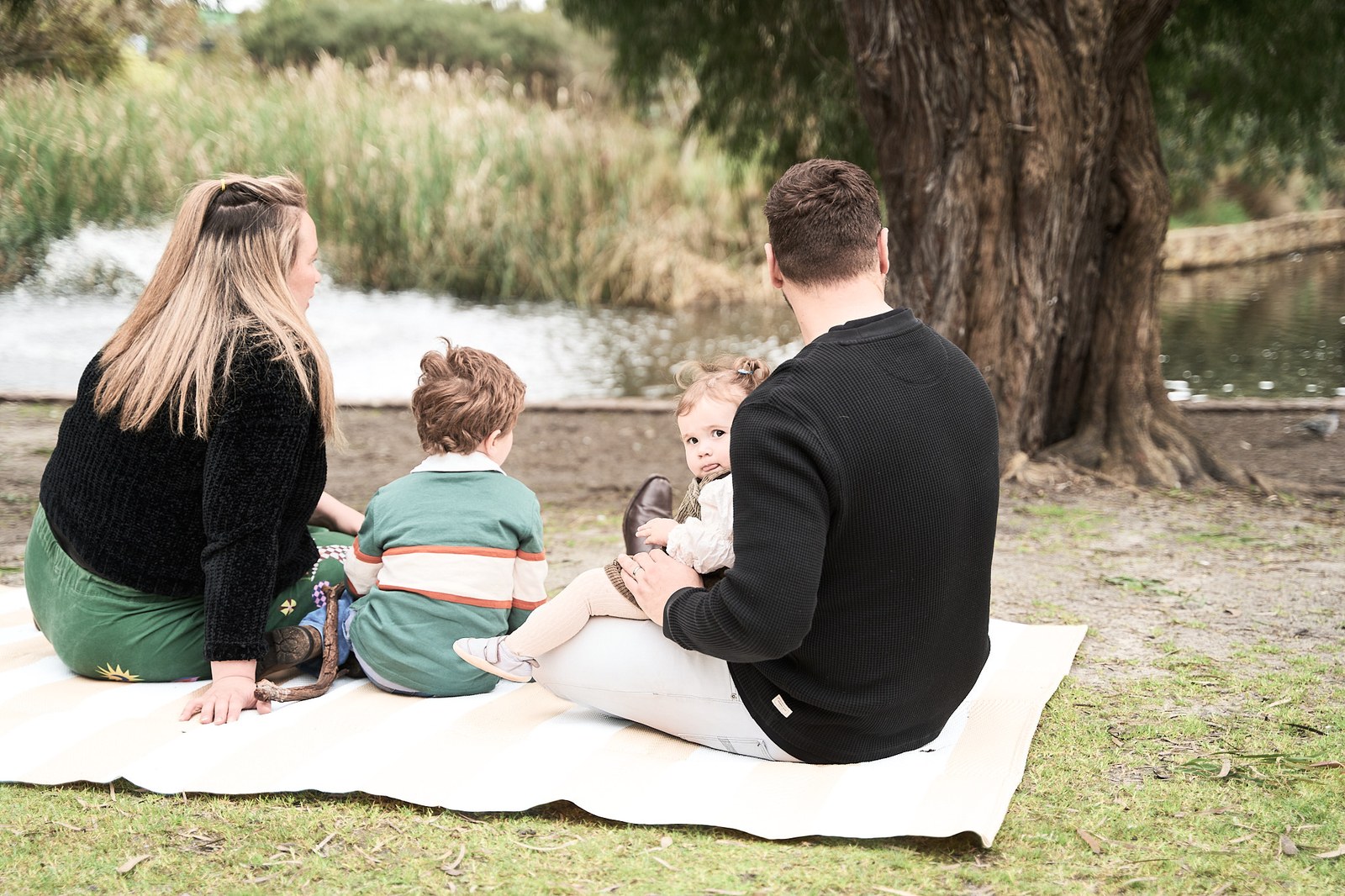 Parents and their two children sitting on a picnic rug by the water