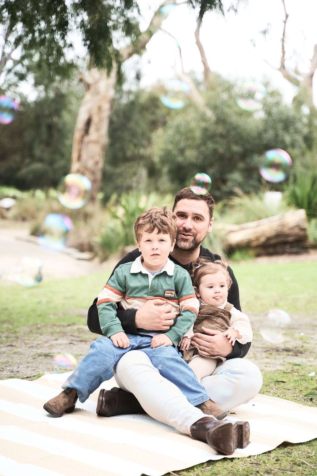 Dad with his son and baby daughter on a rug, bubbles drifting past