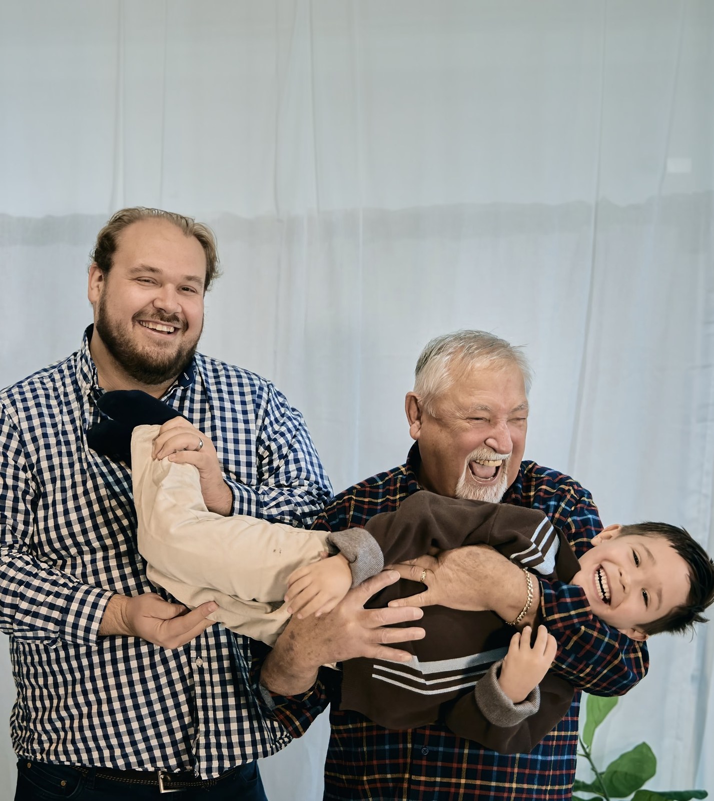 Three generations of men, grandad and dad swinging a laughing boy between them