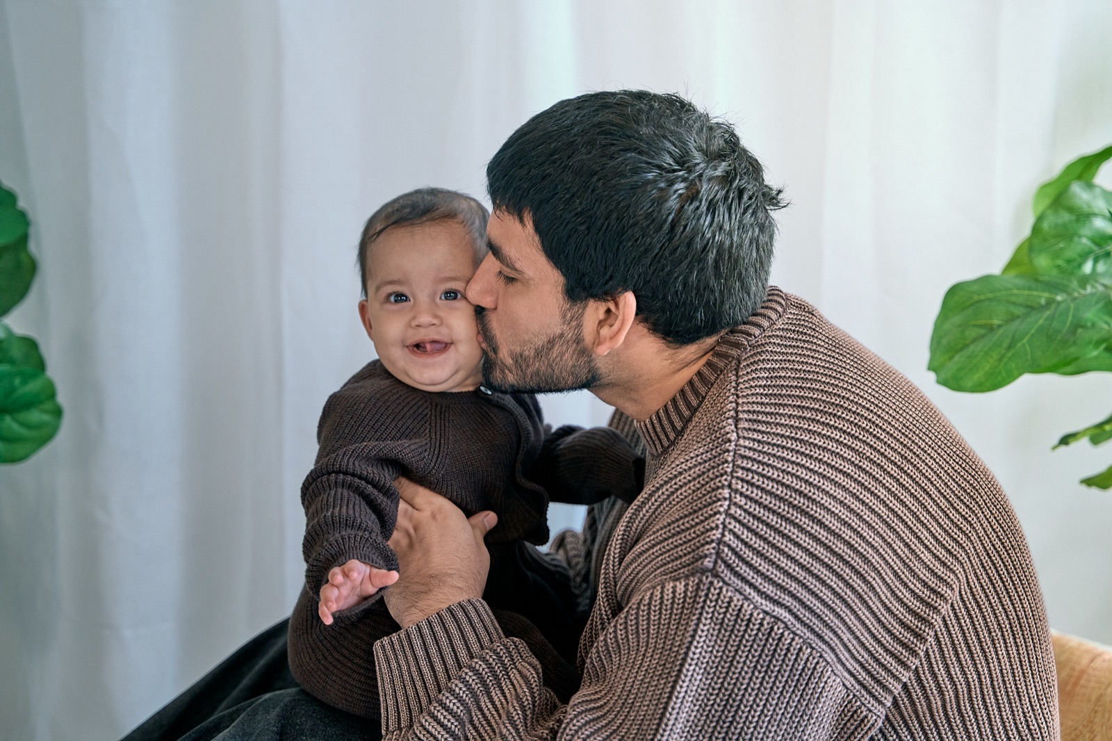 Dad kissing his baby's cheek, both in cosy brown knits