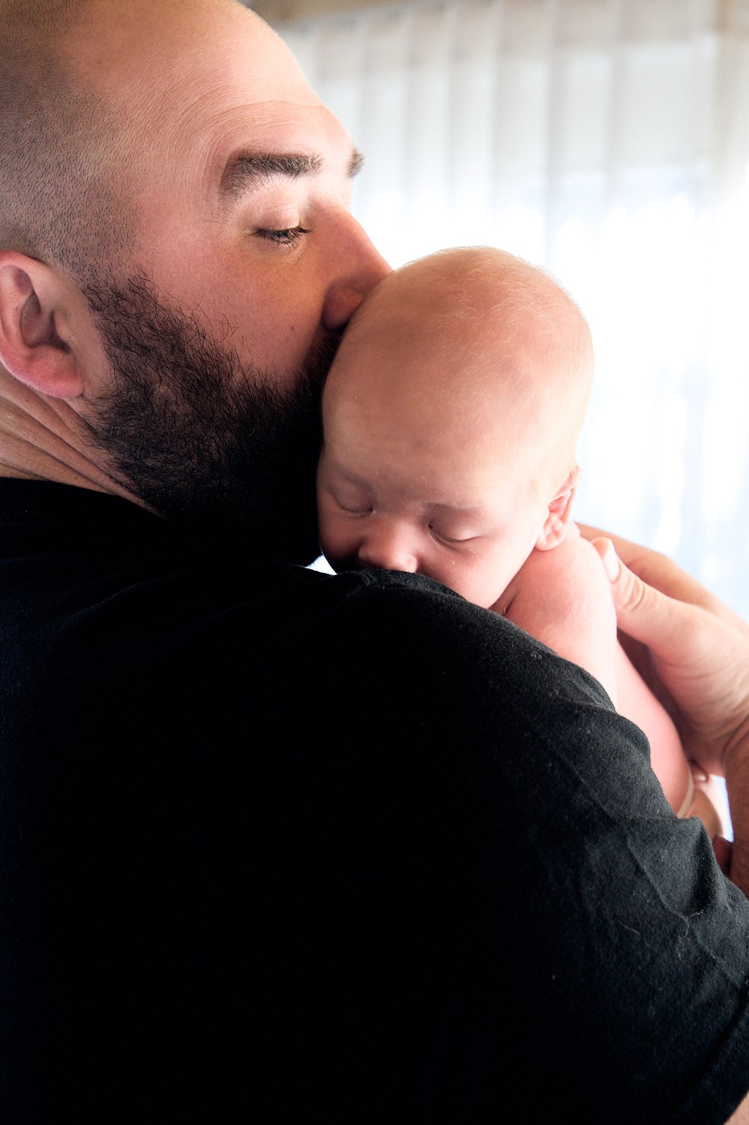 Dad kissing his newborn's head, dark and quiet in-home portrait