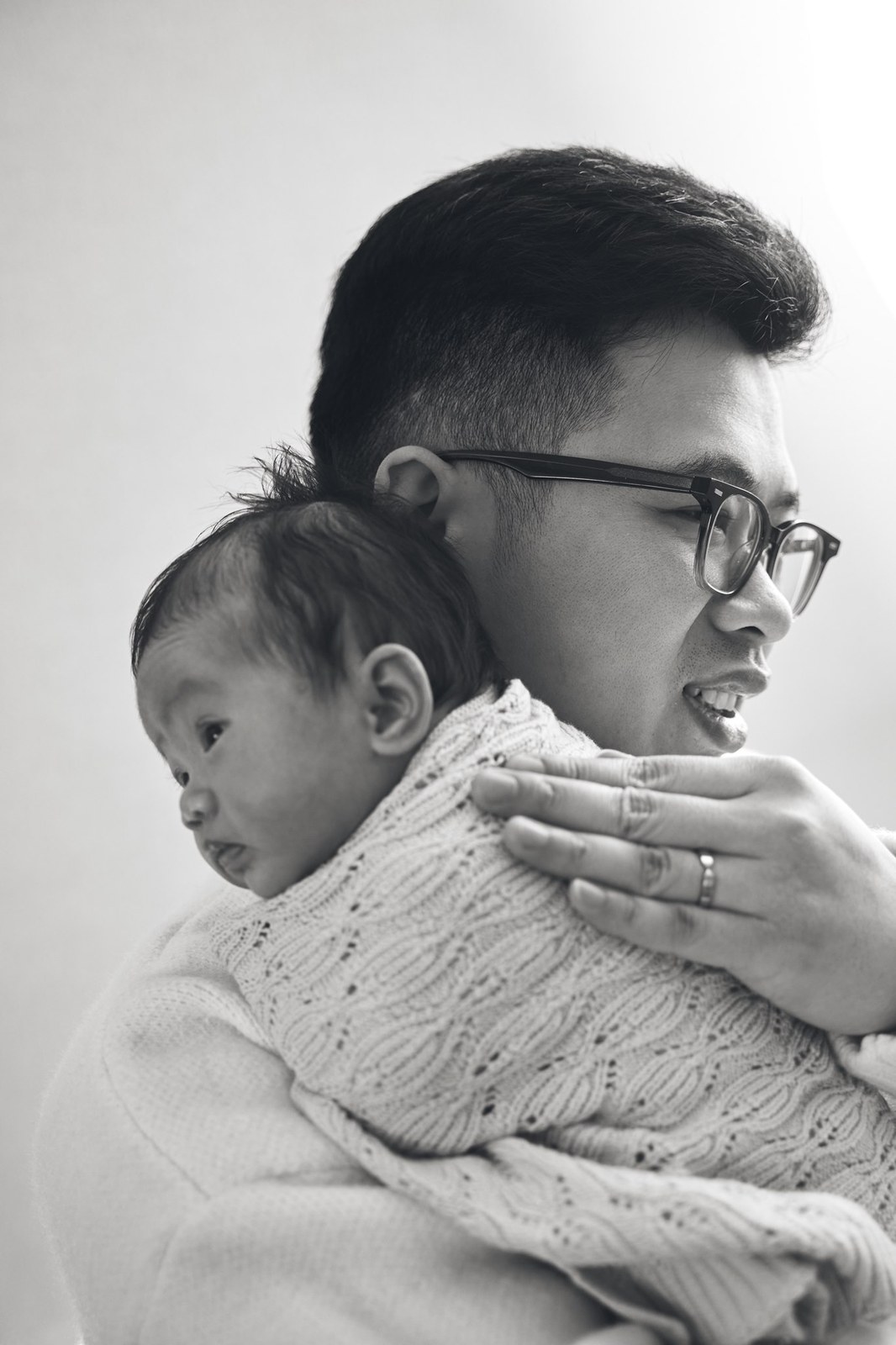 Black and white portrait of a dad with his newborn on his shoulder