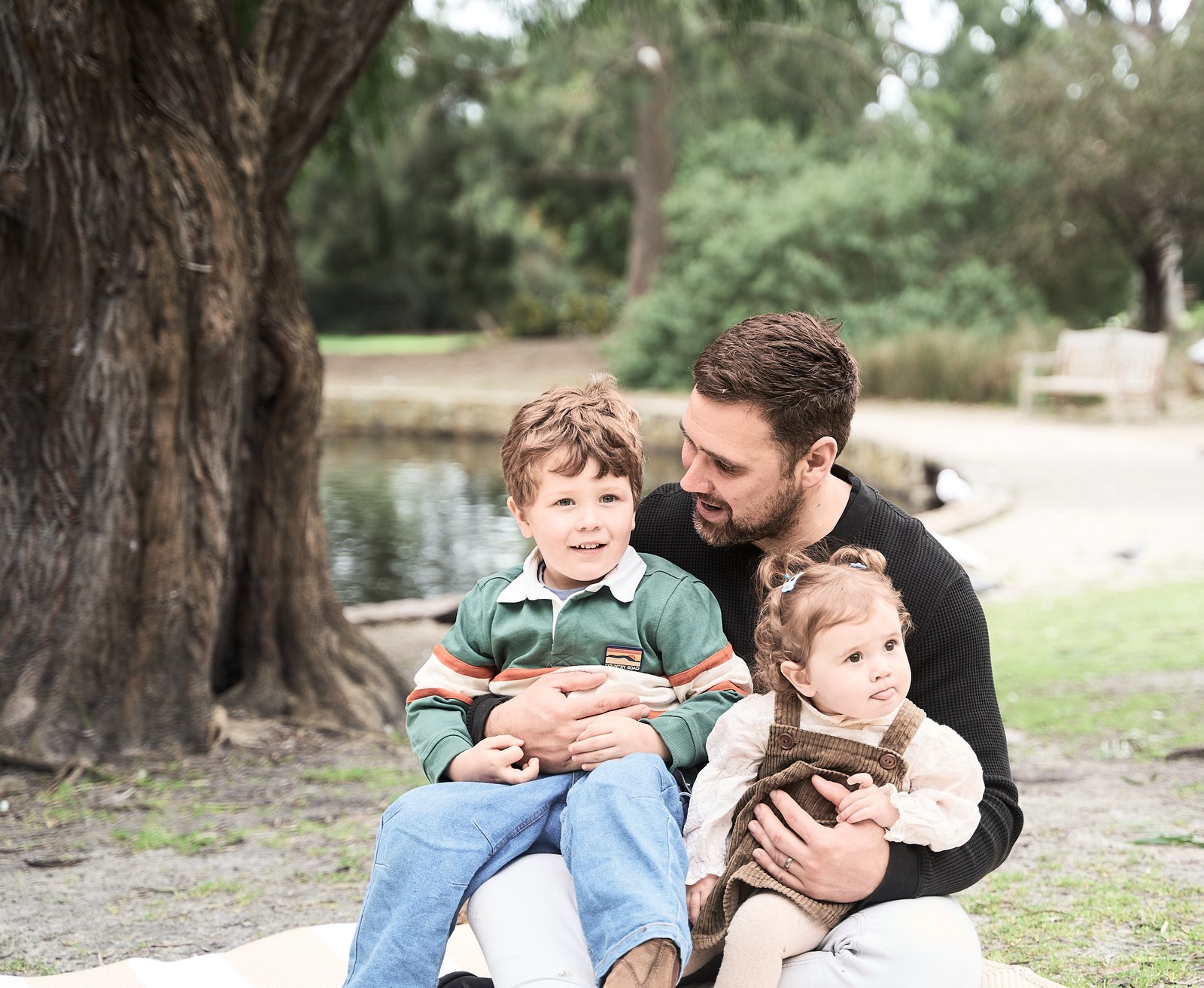 Dad with his son and baby daughter on a rug beside the lake