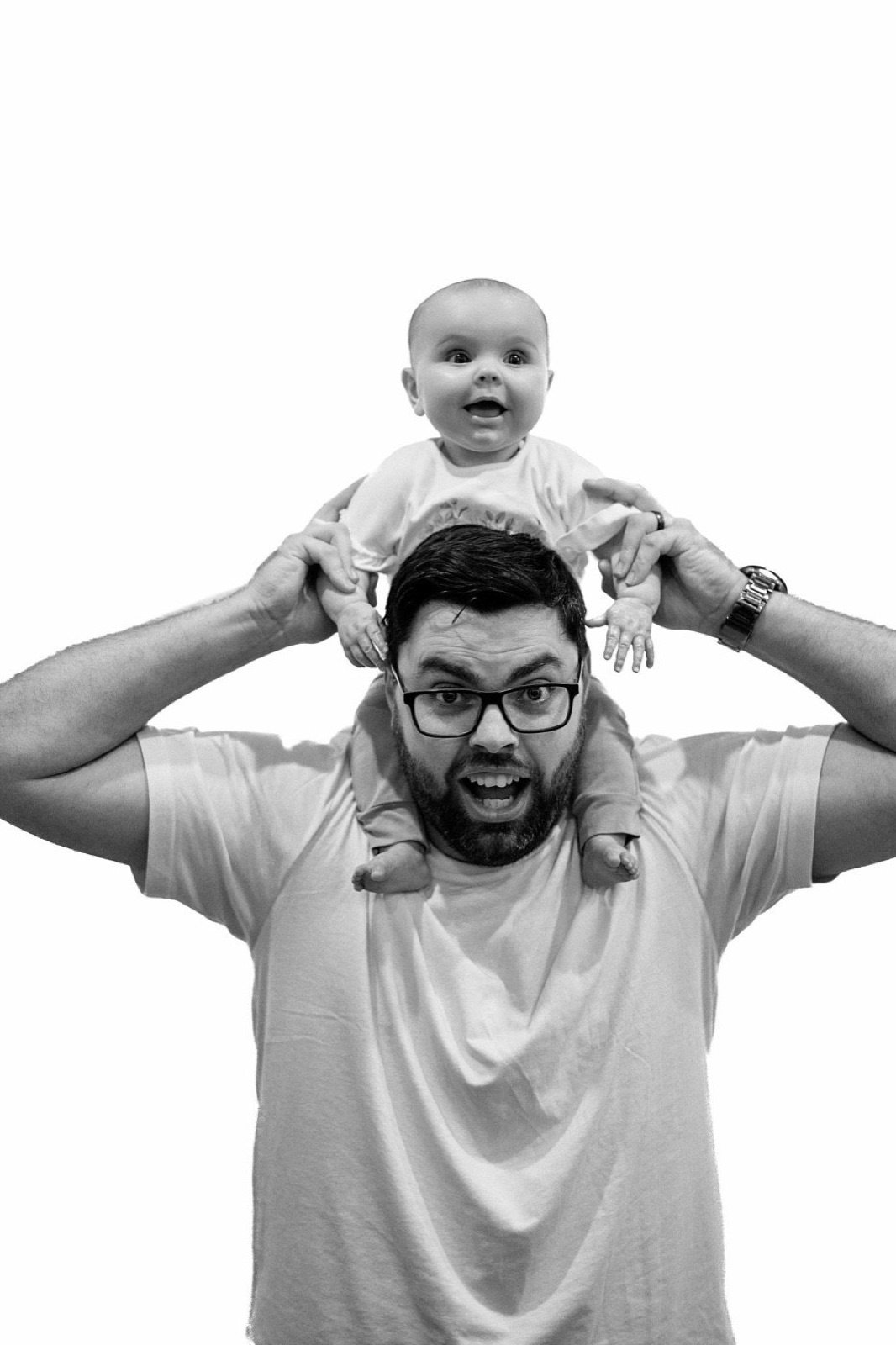 Dad and baby pulling matching faces, baby perched on his shoulders