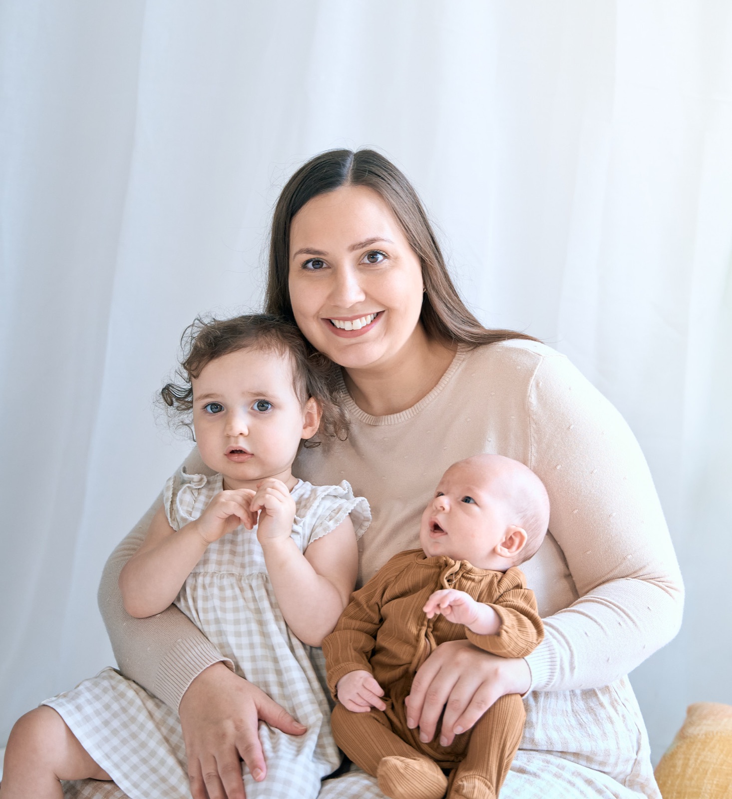 Mum with her baby and a teddy on the bed, soft neutral tones