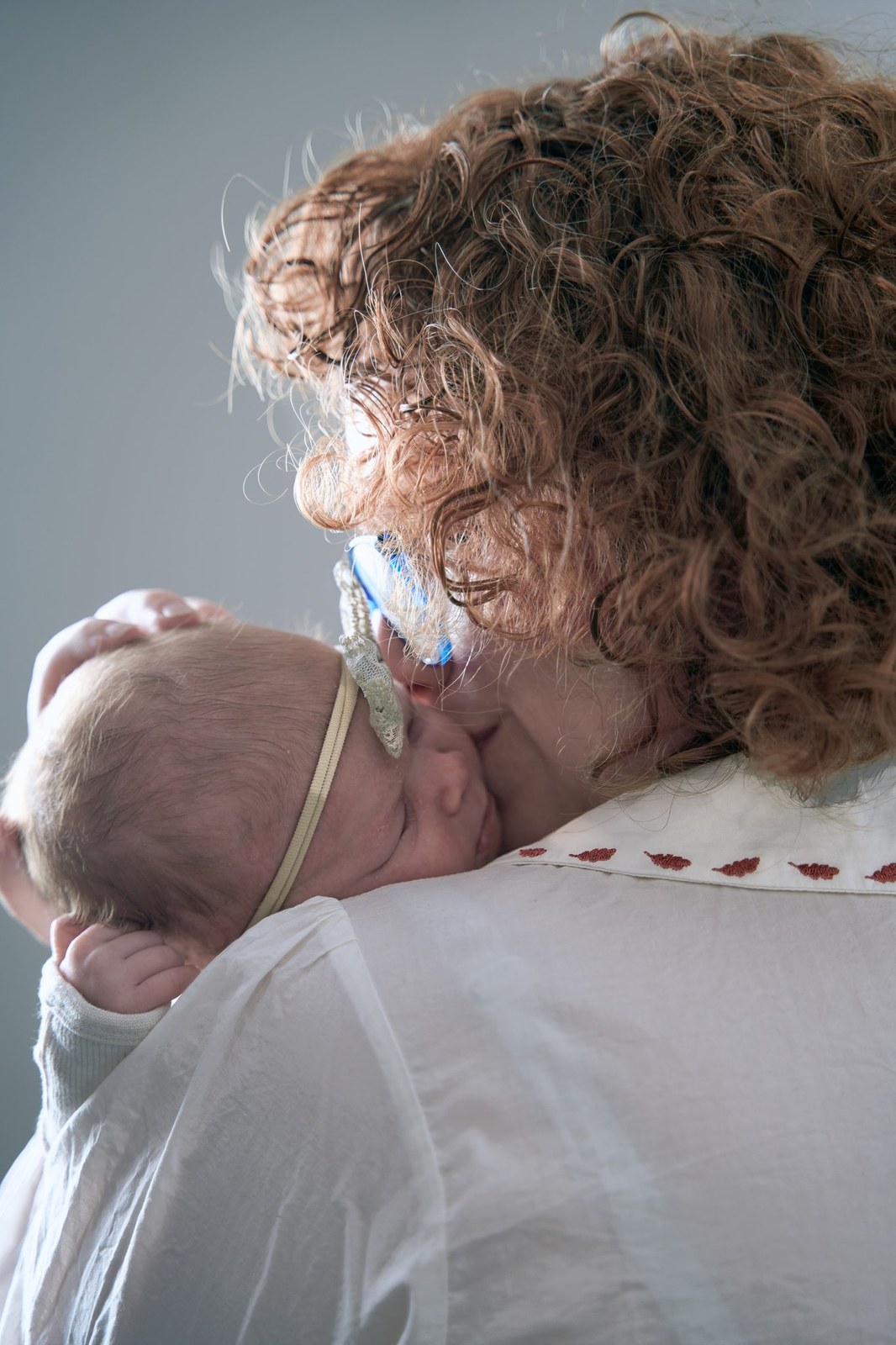 Mum kissing her newborn's head in soft window light