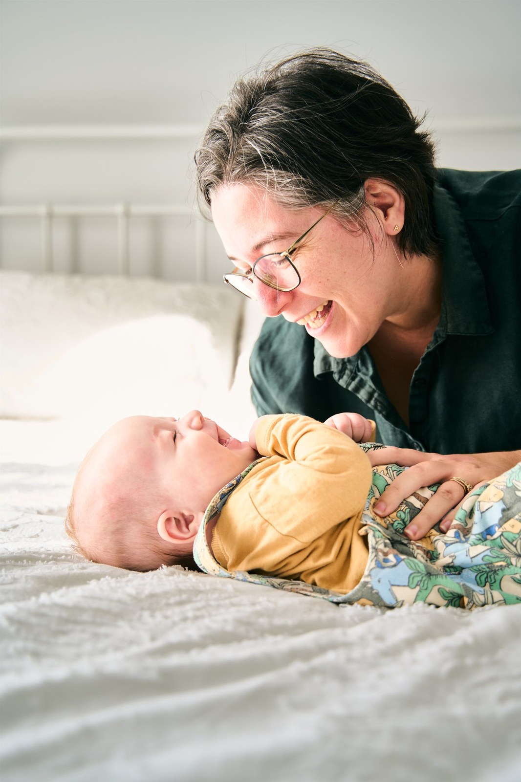 Mum lying beside her baby on the bed, both mid-laugh