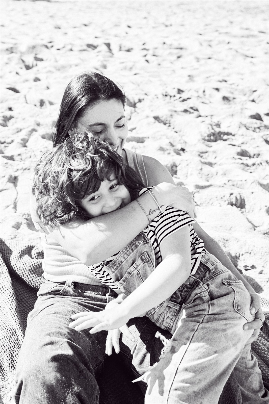 Black and white beach cuddle between mum and her daughter