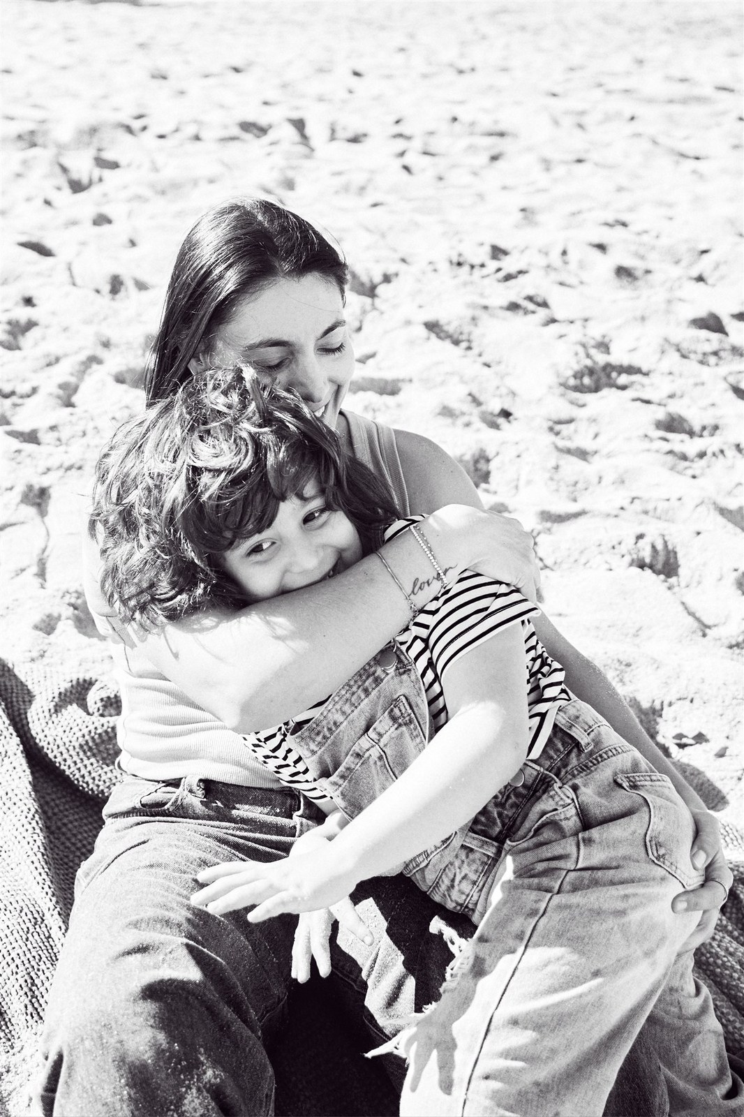 Black and white beach cuddle between mum and her child on the sand