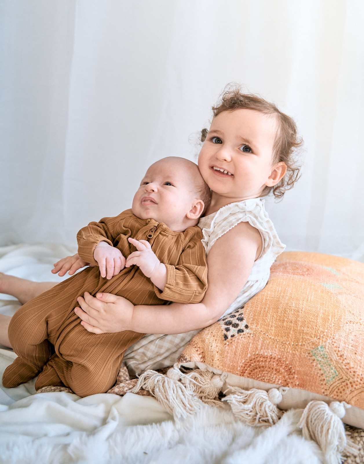 Toddler cuddling her newborn sibling on the bed