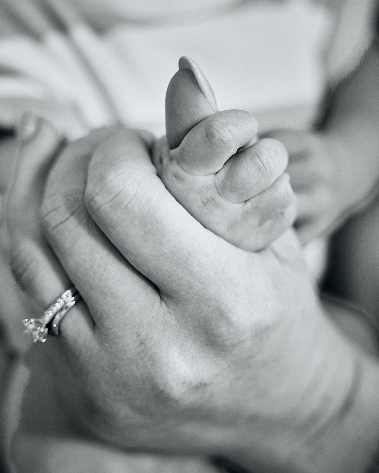 Tiny newborn fist wrapped around mum's thumb, black and white
