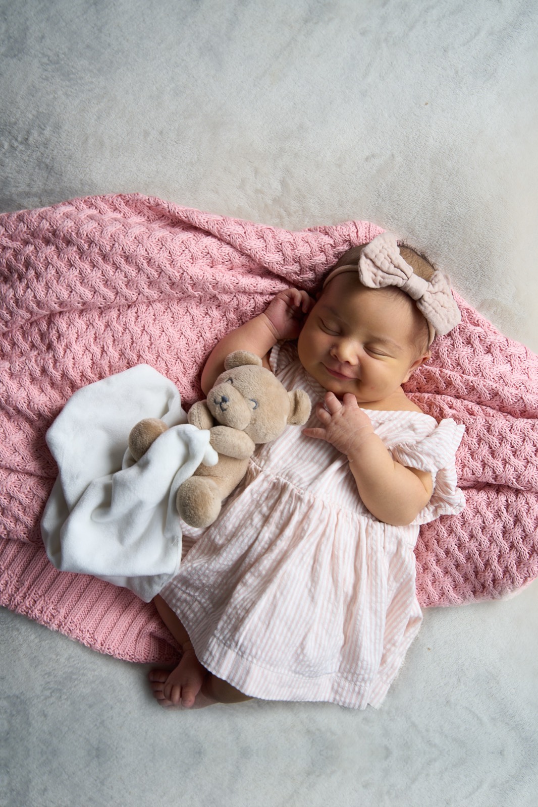 Newborn girl asleep on a pink knit blanket with her teddy