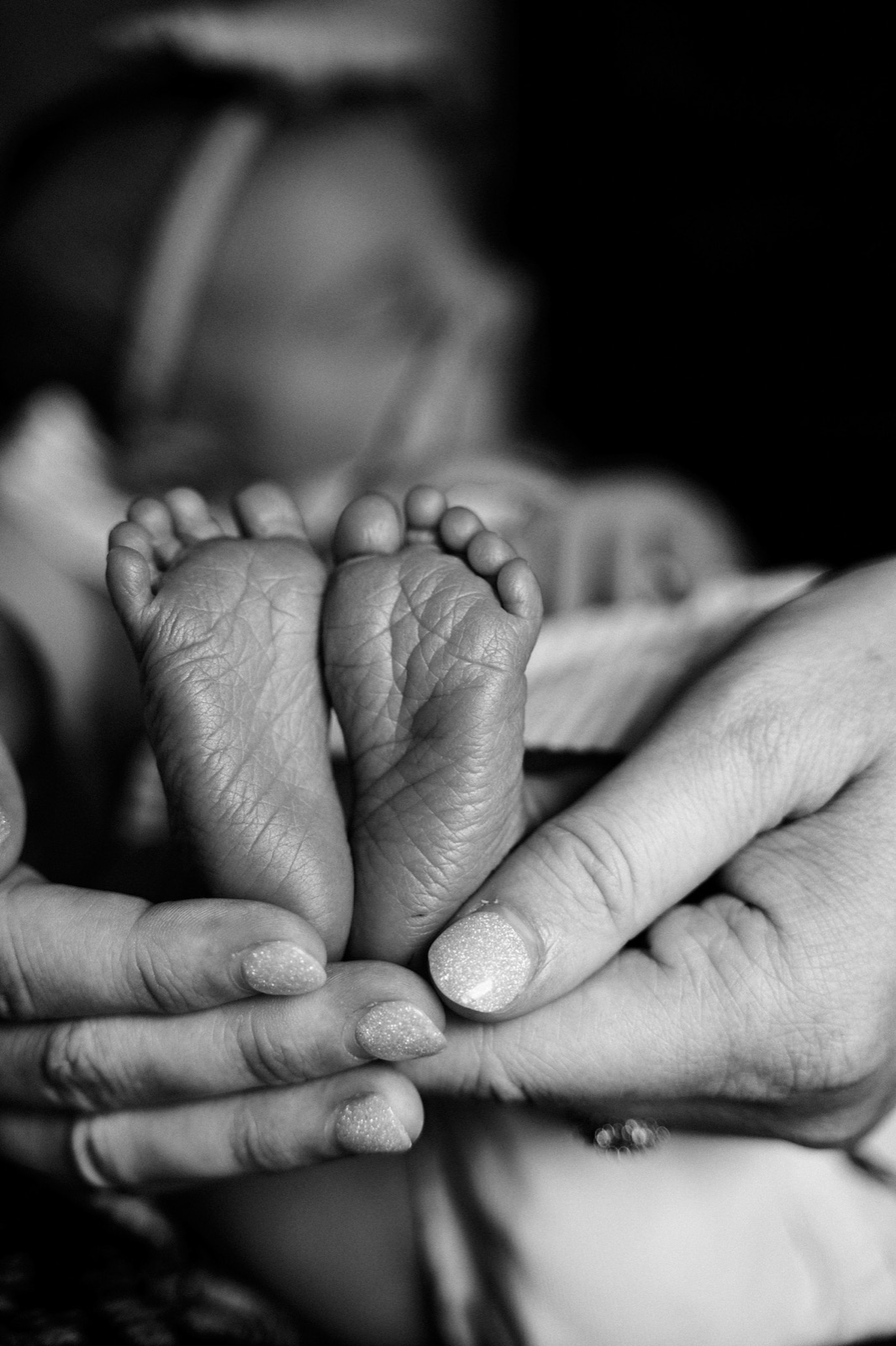 Newborn feet held gently between a parent's fingers, black and white