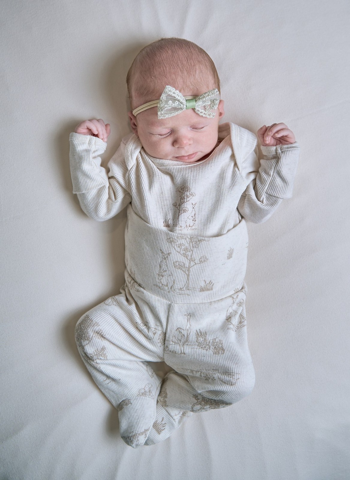 Newborn baby girl asleep on her back in a white romper and bow headband