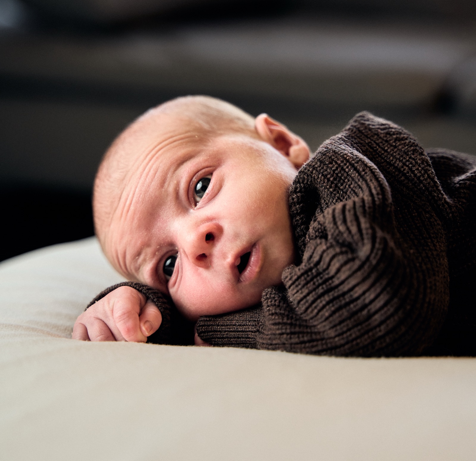 Newborn in a knitted cardigan lifting their head on the bed