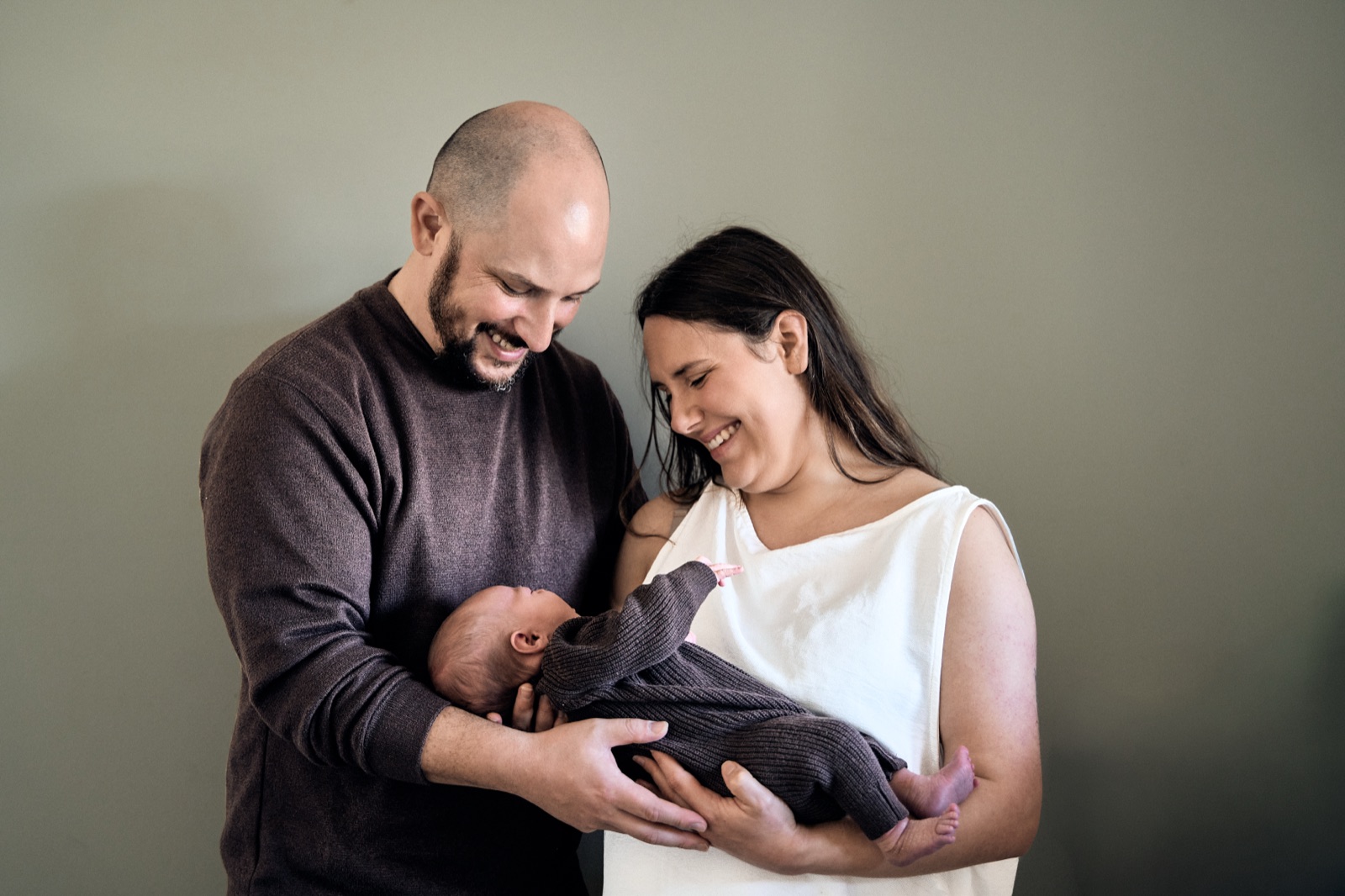 Parents standing in the nursery with their newborn, moody natural light
