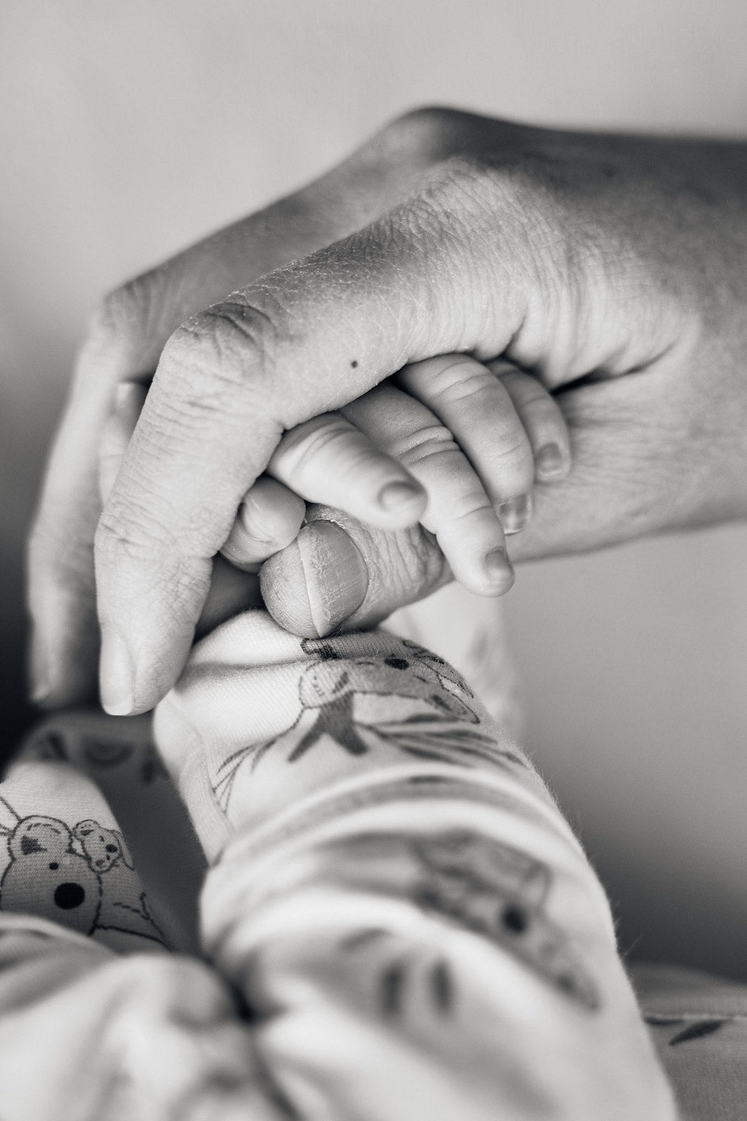 Black and white close-up of a newborn's hand curled around a parent's finger