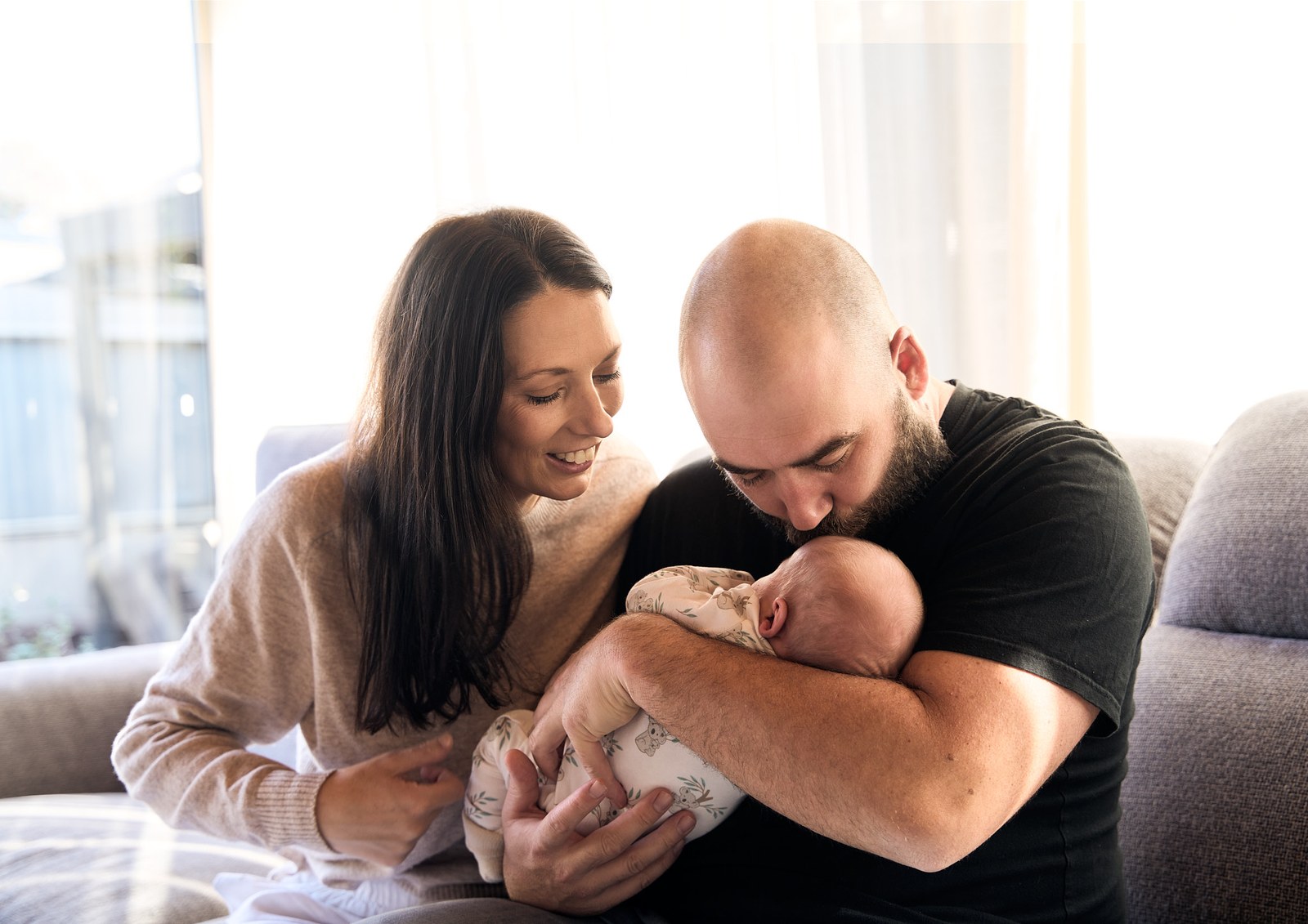 Parents on the couch with their newborn in bright window light