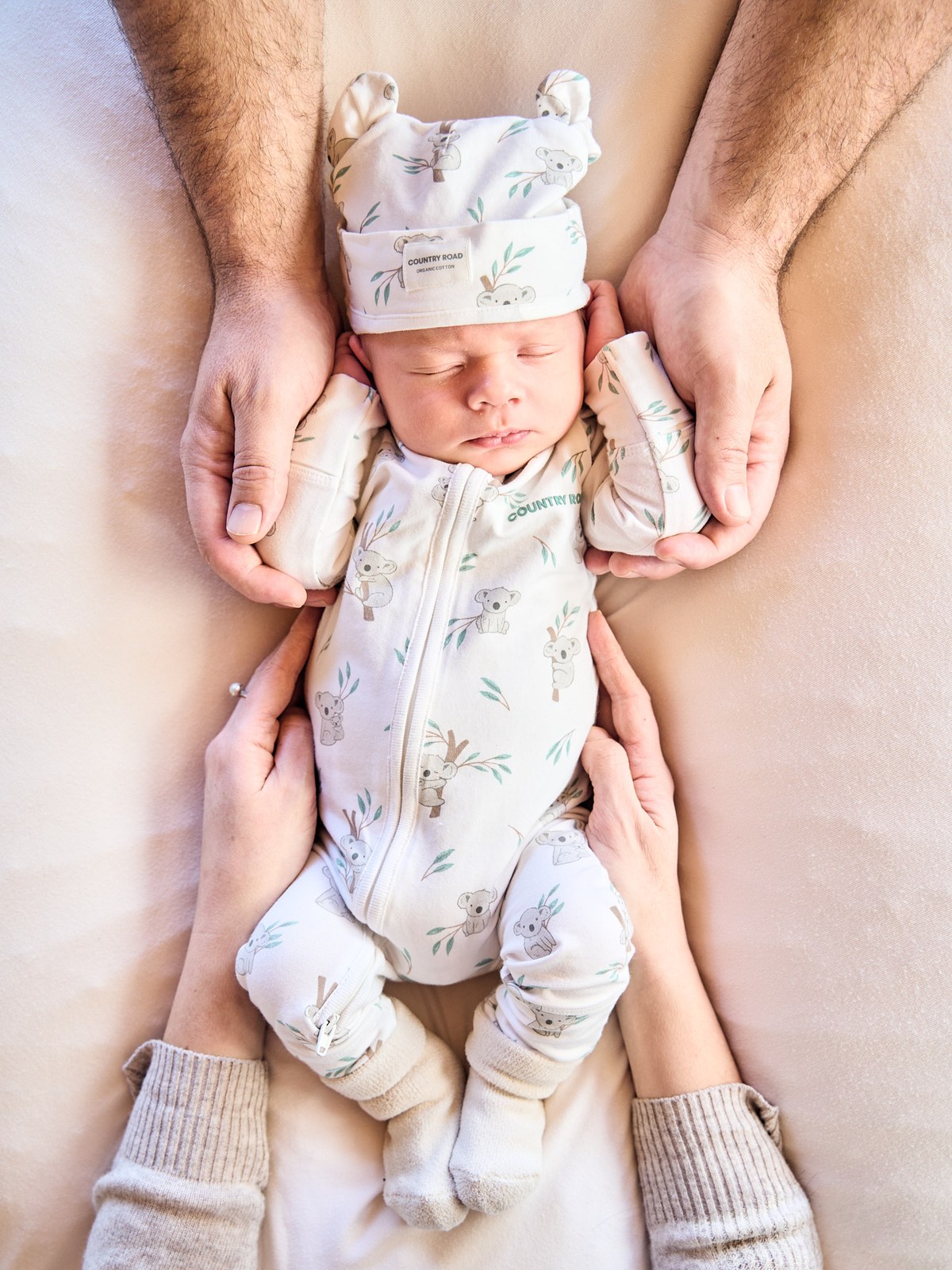 Parents' hands framing their newborn in a bear-ear hat