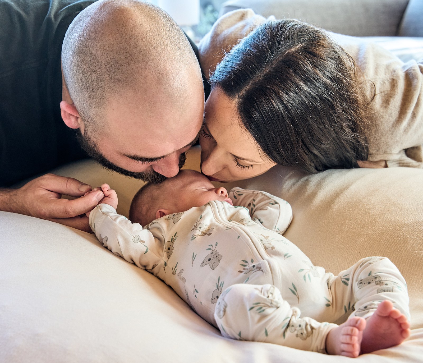 Parents kissing above their sleeping newborn on the bed