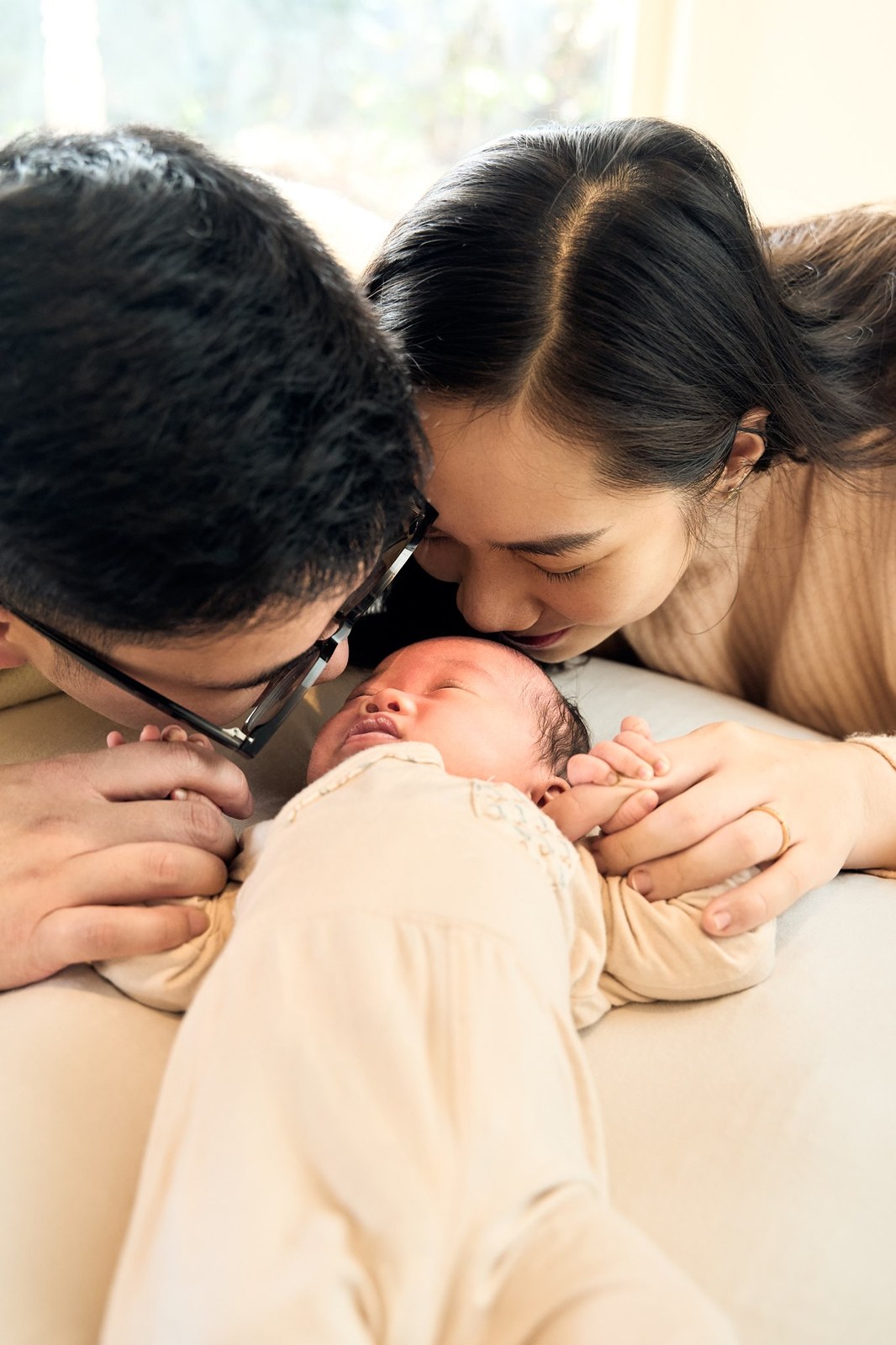 Both parents leaning in to kiss their newborn