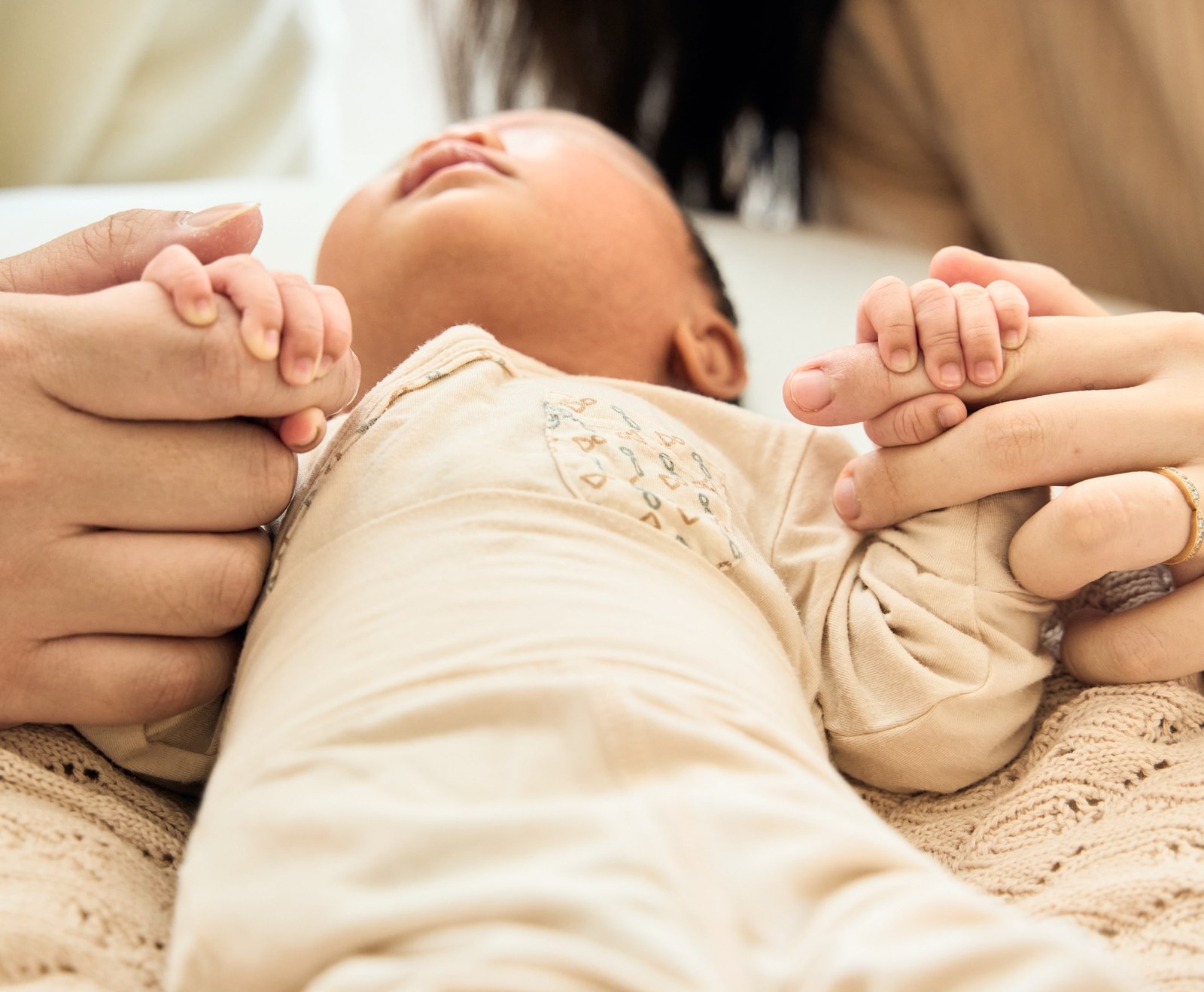 Newborn holding on to both of her parents' fingers