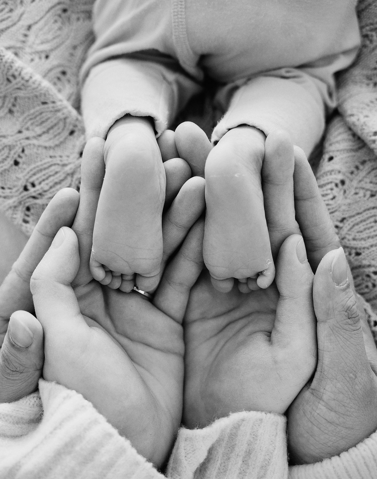 Black and white photo of a newborn's feet cupped in her parents' hands