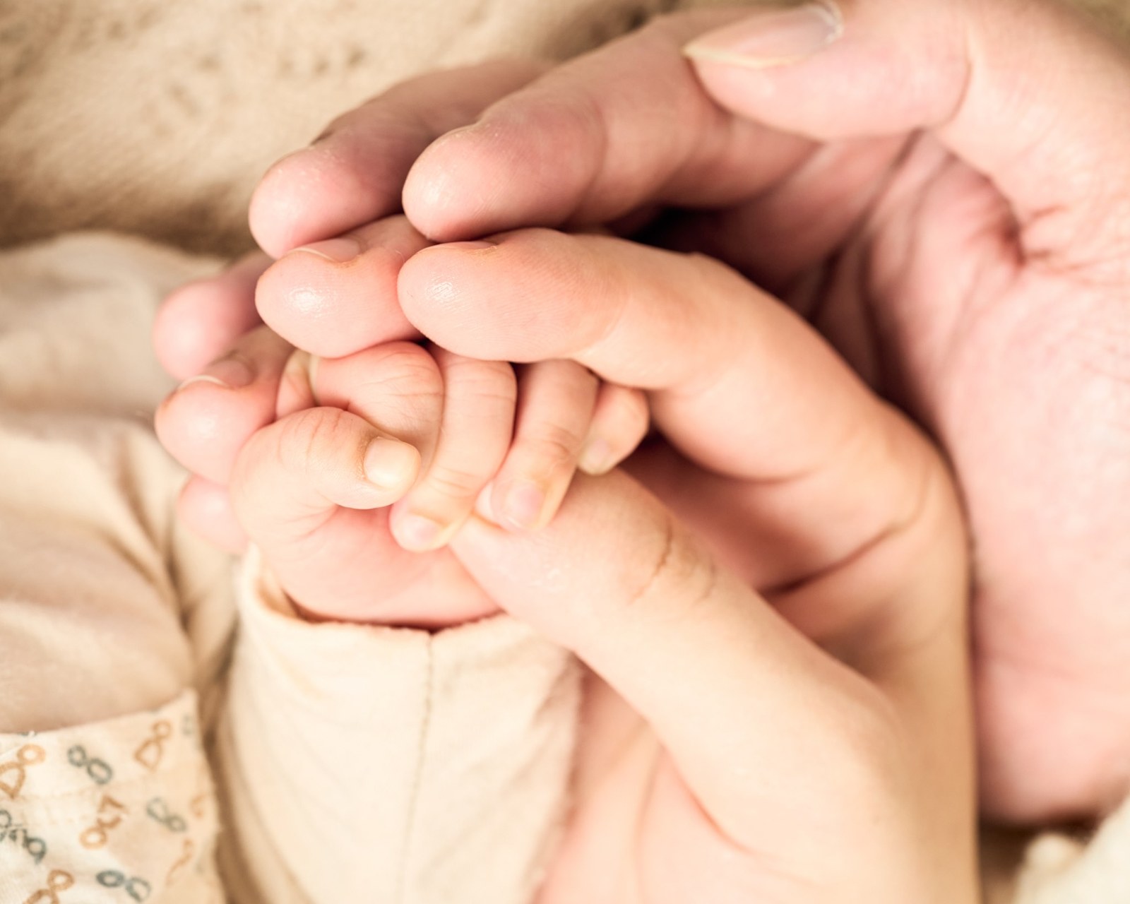 Newborn's hand held between both parents' hands