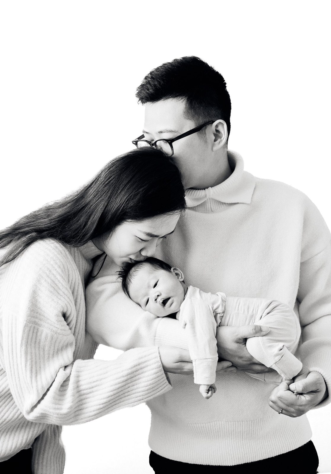 Black and white portrait of parents holding their newborn against a white backdrop