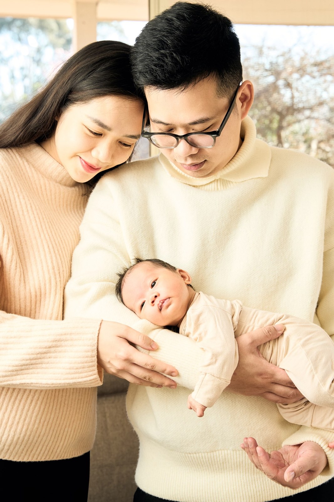 Parents standing by the window with their newborn between them