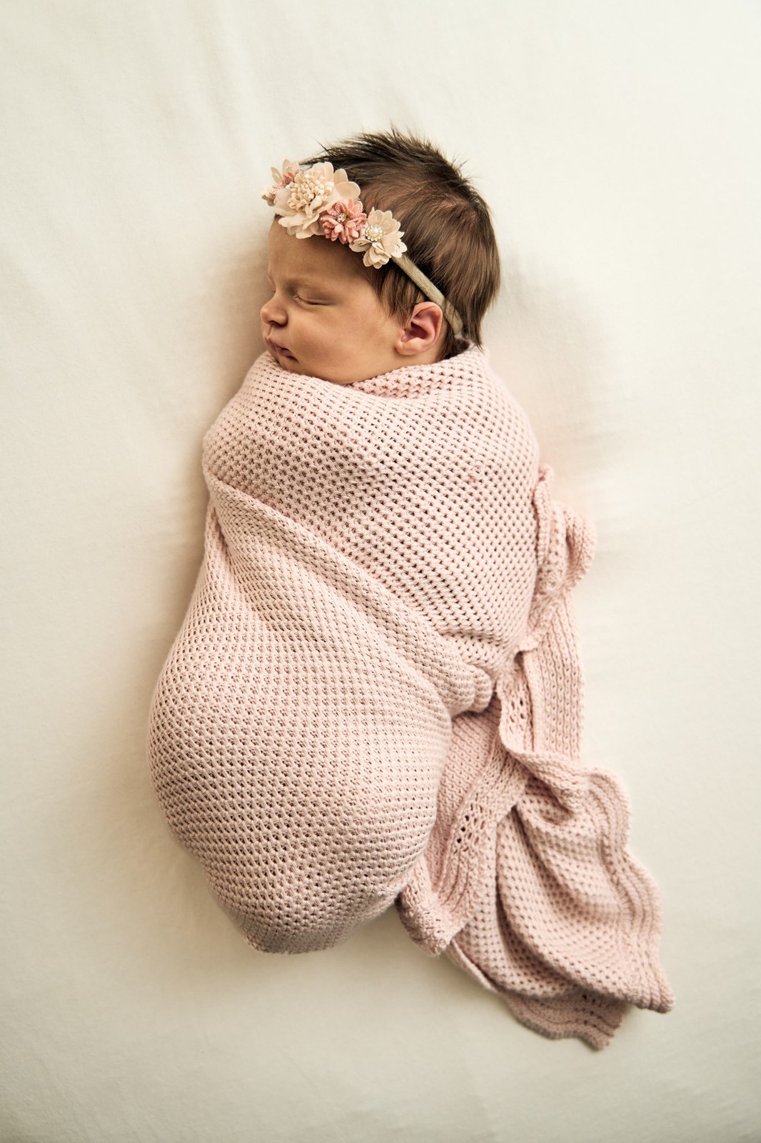 Newborn swaddled in pink with a floral headband