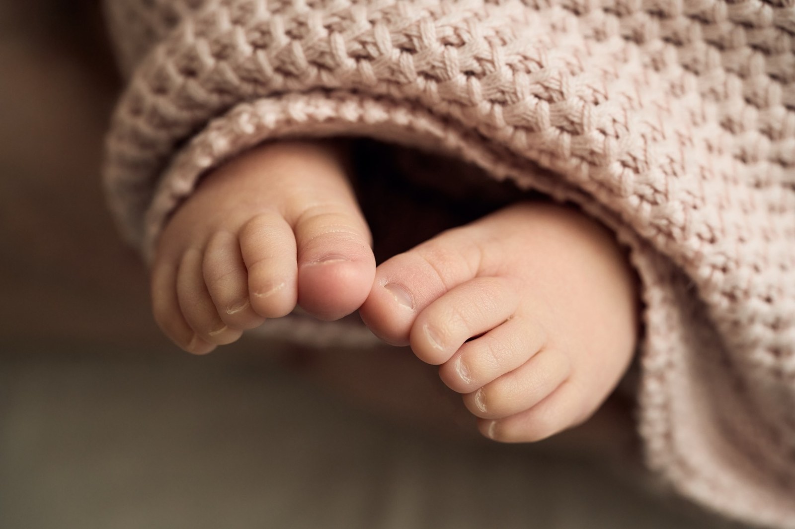 Newborn's feet peeking out from under a pink knitted blanket