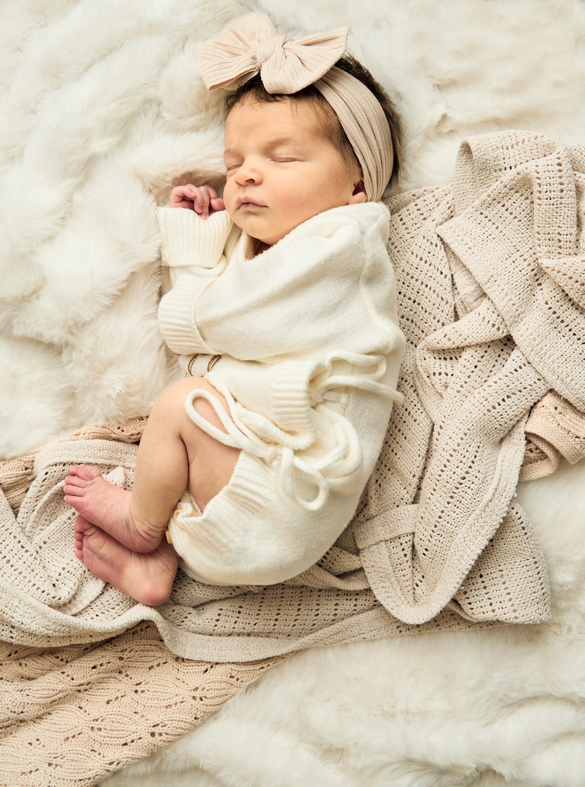 Newborn in cream knit asleep on a soft fur blanket