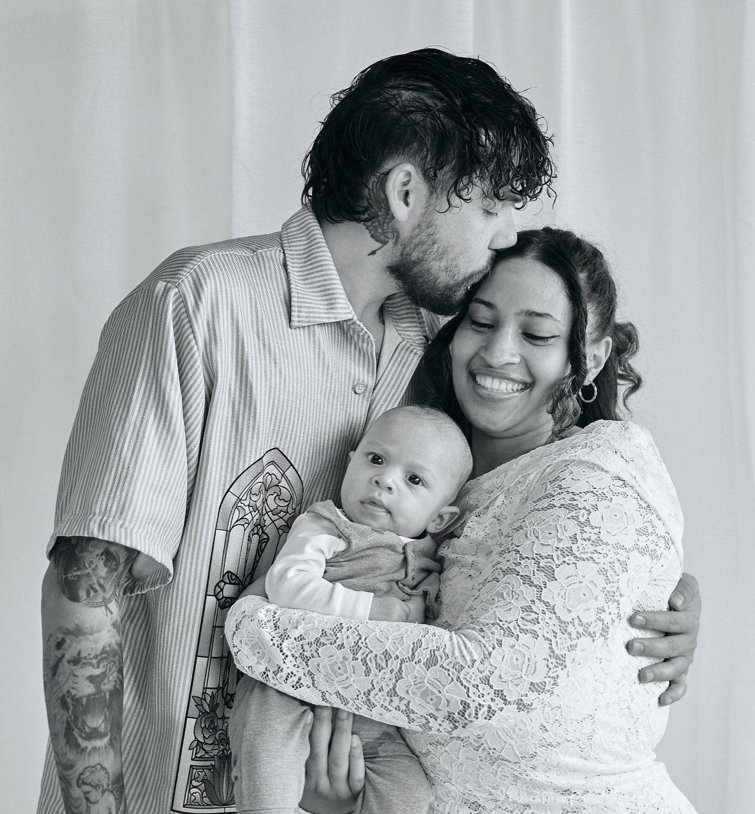 Parents with their newborn wrapped in white, in-home newborn session
