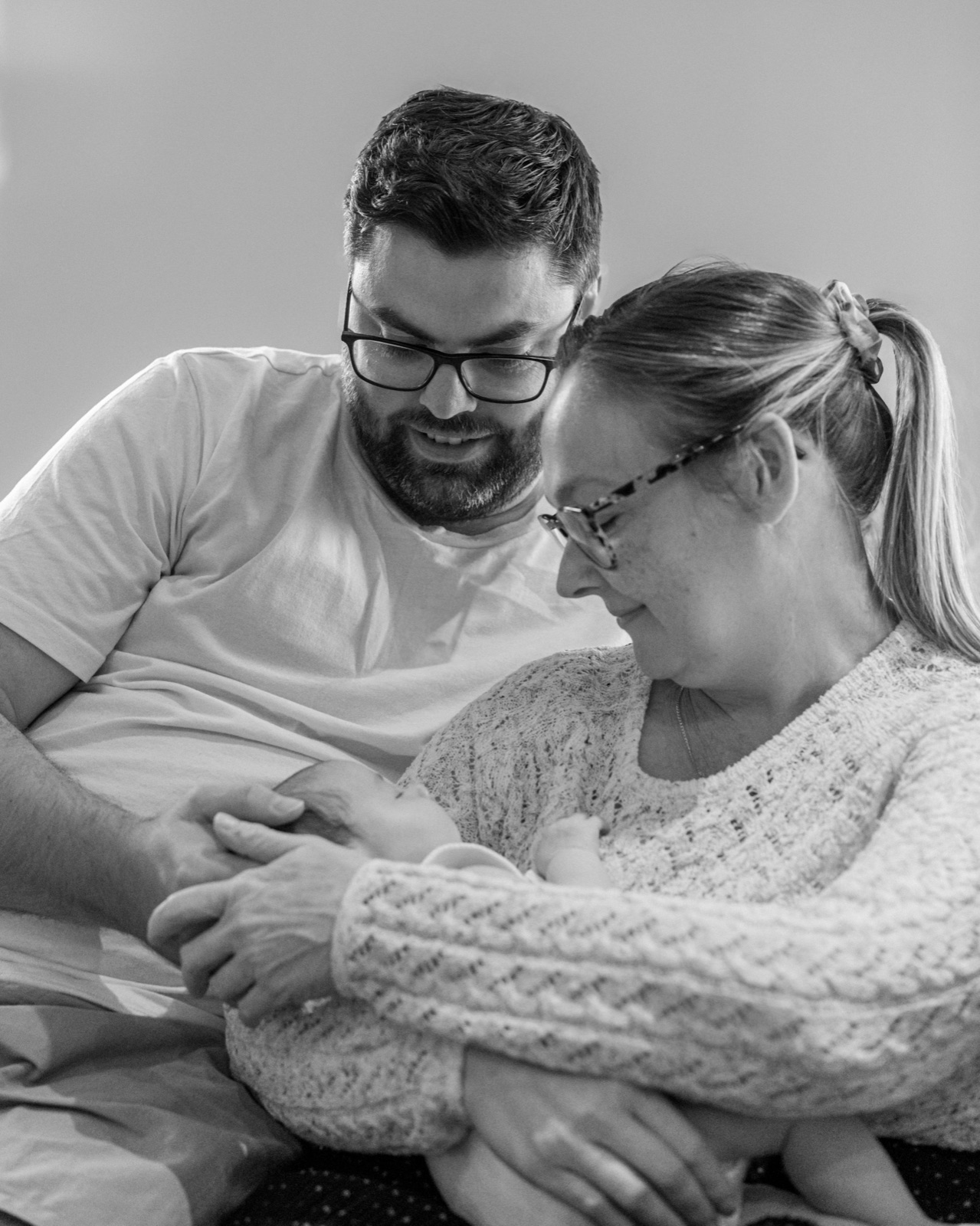 Parents leaning over their newborn together, black and white in-home session